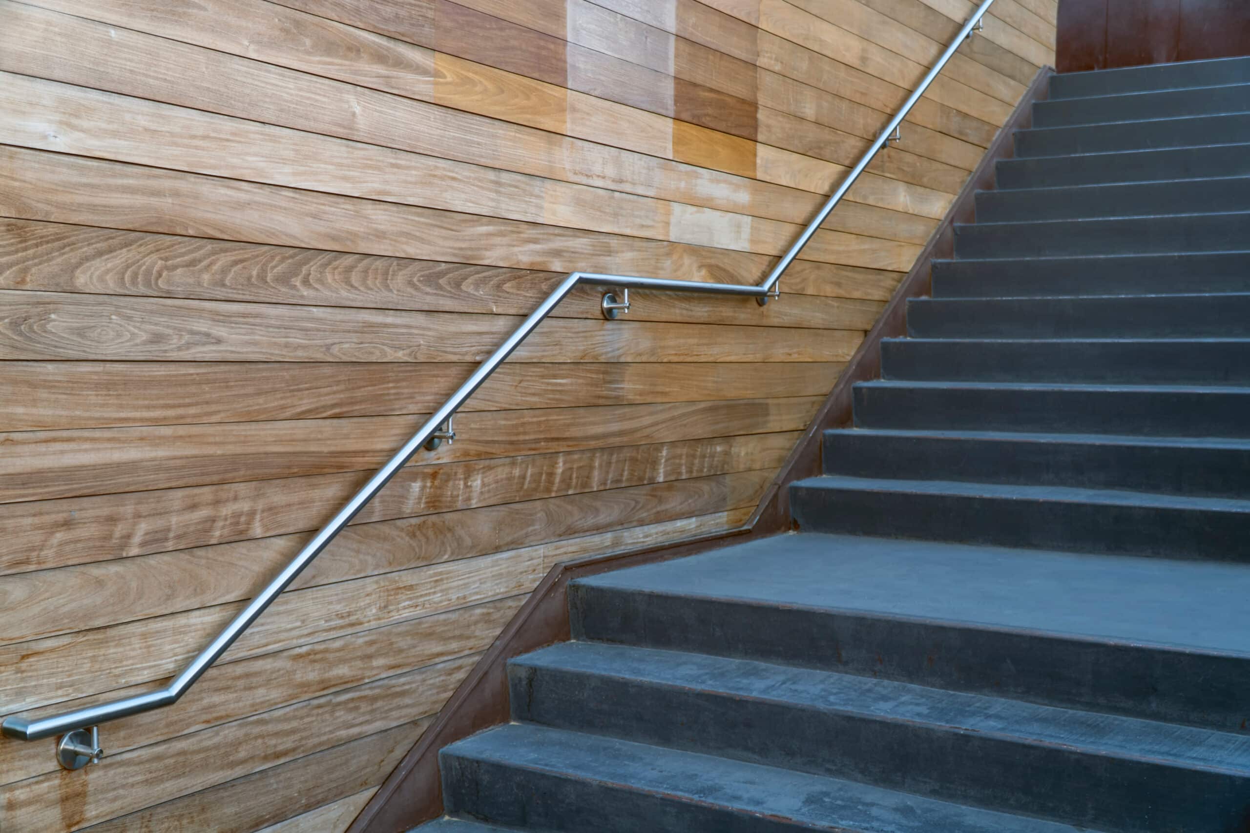 Modern stainless handrail on a decorative wooden wall next to concrete stairs